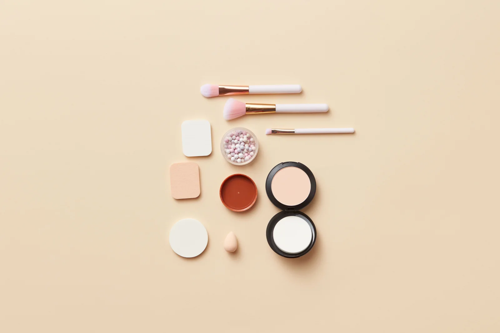 Makeup brushes, powder compacts and sponges arranged on a beige surface